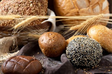 Buğday ve çavdar ekmeği. Kahverengi ahşap bir masada farklı şekillerde çavdar ve buğday ekmeği. Bagetler, somunlar, yuvarlak ekmek, çörekler ve hamburgerler masaya.