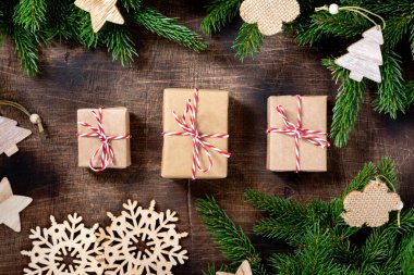 Hediye kutusu. Kahverengi ahşap bir masanın üzerinde el işi kağıt içinde hediye kutuları. Noel arkaplanı hediyeler, köknar dalları ve ahşap tatil süslemeleri. Noel konsepti. Çevre dostu. Üst Manzara. Düz