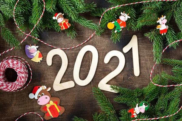 Happy New year 2021 celebration.The number 2021 is made of wood on a brown wooden background. Christmas background with fir branches is decorated with the symbol of 2021 bull cow made of wood. Flatly