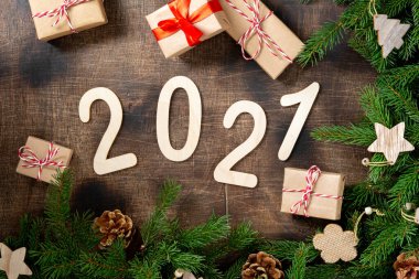 Mutlu yıllar 2021. 2021 numara kahverengi ahşap zemin üzerinde ahşaptan yapılmıştır. Noel arka planında köknar dalları, ahşap dekorlar ve el işi kağıdından hediye kutularıyla süslenir. Düzgünce