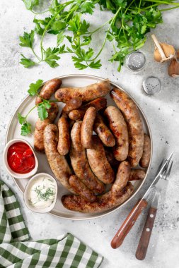 Kızarmış sosis. Baharatlı, soslu, domatesli ve maydanozlu Bavyera ve Nuremberg sosisleri. Açık gri bir masada beyaz seramik tabakta nefis et sosisleri. Alman yemeği.