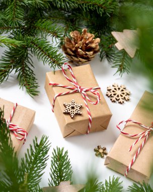 El işi kağıdında hediye kutuları. Noel arkaplanı. Beyaz arka planda ahşap süslemelerle süslenmiş ladin dalları altında Noel hediyeleri