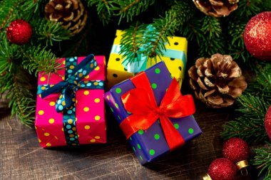 Kahverengi ahşap bir masada farklı renklerde paketlenmiş hediye kutularıyla Noel arkaplanı. Noel ya da yeni yıl hediyeleri köknar dallarının altında