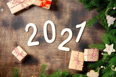 Mutlu yıllar 2021. 2021 numara kahverengi ahşap zemin üzerinde ahşaptan yapılmıştır. Noel arka planında köknar dalları, ahşap dekorlar ve el işi kağıdından hediye kutularıyla süslenir. Düzgünce