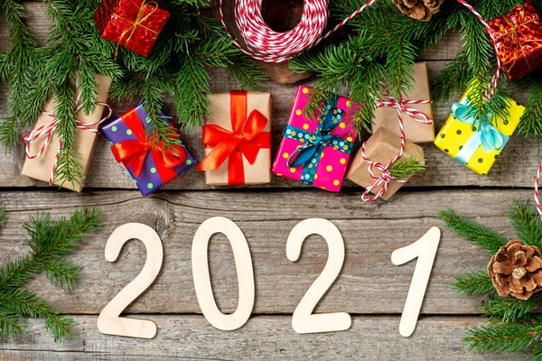 Happy new year 2021. Number 2021 is made of wood on a brown wooden background. Christmas background with fir branches decorated with cones. Flatly
