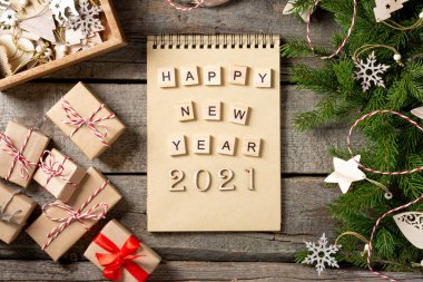 Mutlu yıllar 2021. 2021 numara kahverengi ahşap zemin üzerinde ahşaptan yapılmıştır. Noel arka planında köknar dalları, ahşap dekorlar ve el işi kağıdından hediye kutularıyla süslenir. Düzgünce