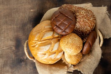 Buğday ve çavdar ekmeği. Açık gri bir masada farklı şekillerde çavdar ve buğday ekmeği. Masada yuvarlak buğday ekmeği, çörek ve hamburgerler var..