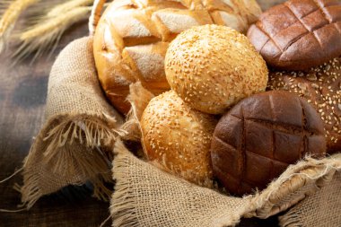 Buğday ve çavdar ekmeği. Açık gri bir masada farklı şekillerde çavdar ve buğday ekmeği. Masada yuvarlak buğday ekmeği, çörek ve hamburgerler var..