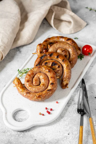 Açık gri bir masada servis panosunda tütsülenmiş sosis. Spiral sosisler. Ev yapımı kızarmış sosis.