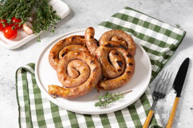 Açık gri bir masada servis panosunda tütsülenmiş sosis. Spiral sosisler. Ev yapımı kızarmış sosis.