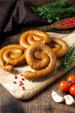 Kahverengi ahşap bir masada servis panosunda tütsülenmiş sosis. Spiral sosisler. Ev yapımı kızarmış sosis.