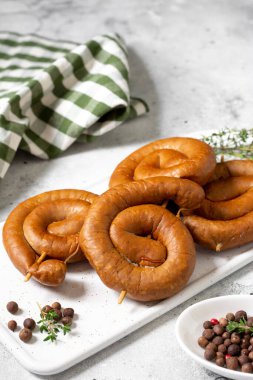 Açık gri bir masada servis panosunda tütsülenmiş sosis. Spiral sosisler. Ev yapımı kızarmış sosis.