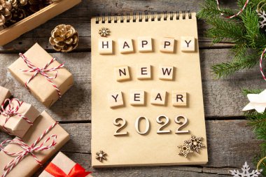 Mutlu yıllar 2022. 2022 numara kahverengi ahşap zemin üzerinde ahşaptan yapılmıştır. Noel arka planında köknar dalları, ahşap dekorlar ve el işi kağıdından hediye kutularıyla süslenir. Düzgünce