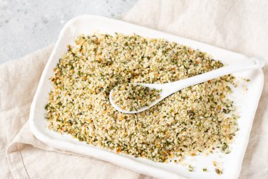 Kenevir tohumları. Açık gri mutfak masasında beyaz bir seramik kasede kurutulmuş kenevir tohumları. Pişirmek için kenevir tohumları