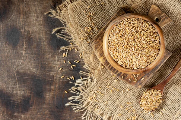 茶色の木製のテーブルの上に木製のボウルに小麦をつづった 健康的な食事のための呪文のシリアル文化 — ストック写真