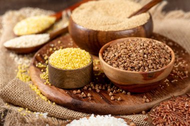 Beyaz ve kırmızı pirinç, karabuğday, amaranth tohumu, mısır homurtusu, kinoa ve darı kahverengi ahşap bir masada kaselerde. Glütensiz tahıllar