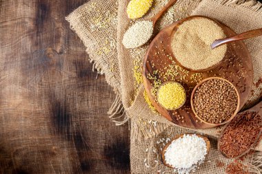 Beyaz ve kırmızı pirinç, karabuğday, amaranth tohumu, mısır homurtusu, kinoa ve darı kahverengi ahşap bir masada kaselerde. Glütensiz mısır gevreği. Kopyalama alanı olan üst görünüm