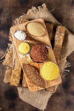 Beyaz ve kırmızı pirinç, karabuğday, amaranth tohumu, mısır homurtusu, kinoa ve darı kahverengi ahşap bir masada kaselerde. Glütensiz mısır gevreği. Kopyalama alanı olan üst görünüm