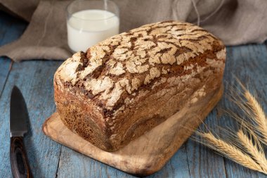 Servis tahtasında ayçekirdeği olan çavdar ekmeği. Tahtadaki ekmek parçaları ve ahşap bir kırsal masada bir bardak süt. Sağlıklı çavdar ekmeği