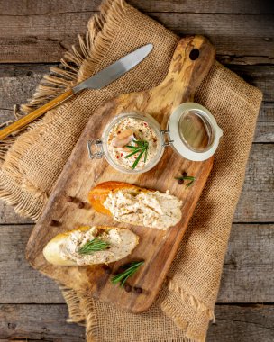Kahverengi ahşap mutfak masasında cam bir kavanozda tavuk ezmesi. Ahşap arka planda baharatlı ev yapımı tavuk filetosu. Tavuklu baget parçaları servis tahtasına serpilmiş.