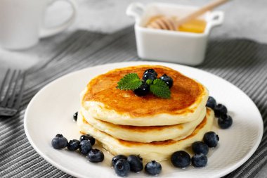 Açık gri mutfak masasında beyaz tabakta krep. Ballı ve yaban mersinli ev yapımı lezzetli krepler. Lezzetli tatlı ve doyurucu bir kahvaltı.