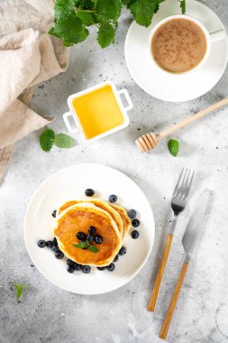 Açık gri mutfak masasında beyaz tabakta krep. Ballı ve yaban mersinli ev yapımı lezzetli krepler. Lezzetli tatlı ve doyurucu bir kahvaltı.