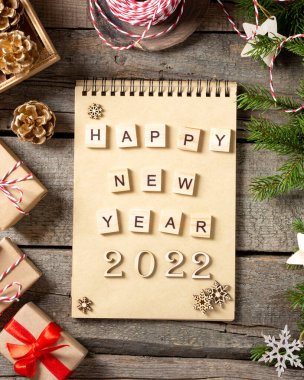 Mutlu yıllar 2022. 2022 numara kahverengi ahşap zemin üzerinde ahşaptan yapılmıştır. Noel arka planında köknar dalları, ahşap dekorlar ve el işi kağıdından hediye kutularıyla süslenir. Düzgünce