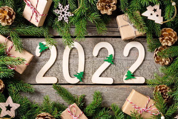 Happy New Year 2022. Number 2022 is made of wood on a wooden background. Christmas background with fir branches. ECO decorations