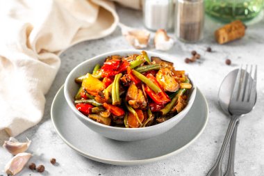 Açık gri mutfak masasında gri bir kasede sebze turşusu. Farklı sebzeler, kırmızı biber, patlıcan, havuç ve bezelye. Vejetaryen yemeği.