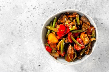 Açık gri mutfak masasında gri bir kasede sebze turşusu. Farklı sebzeler, kırmızı biber, patlıcan, havuç ve bezelye. Vejetaryen yemeği.