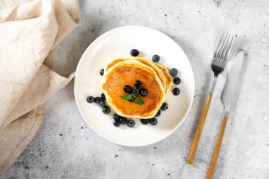 Açık gri mutfak masasında beyaz tabakta krep. Ballı ve yaban mersinli ev yapımı lezzetli krepler. Lezzetli tatlı ve doyurucu bir kahvaltı.