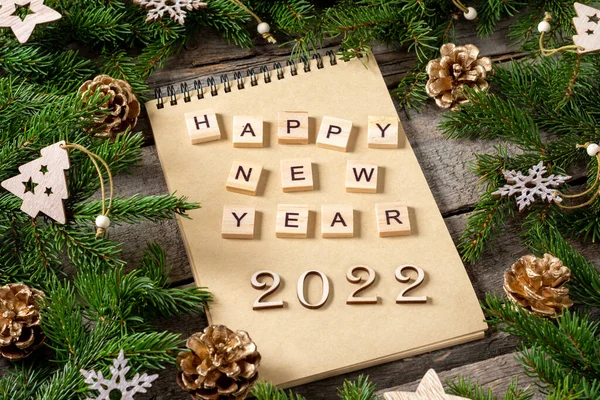 Happy new year 2022. Number 2022 is made of wood on a brown wooden background. Christmas background with fir branches is decorated with wooden decor and gift boxes made of craft paper. Flatly