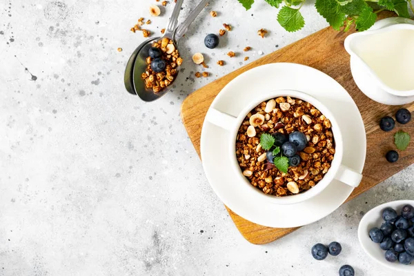 Karabuğdaydan yapılmış ev yapımı granola. Organik karabuğday taneleri, yeşil karabuğday filizleri, fındık, kabak tohumu, keten tohumu ve hindistan cevizi. Açık gri mutfak masasında beyaz bir tabakta granola.