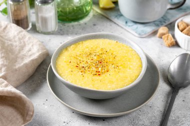 Açık gri mutfak masasında seramik tabakta mısır lapası. Baharatlı yulaf lapası. Kremalı polenta çorbası. Sağlıklı vejetaryen kahvaltısı