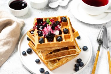 Yunan yoğurdu ve böğürtlen reçelli Belçika ya da Brüksel waffle 'ı. Açık gri mutfak masasında beyaz tabakta ev yapımı waffle 'lar. Geleneksel klasik Belçika waffleları