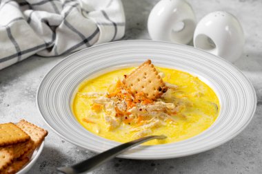 Kremalı et suyunda tavuk göğsü. Sebzeli ve kremalı tavuk. Açık gri mutfak masasında bir kasede tavuk çorbası.