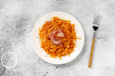 Ağır ateşte pişmiş lahana. Açık gri mutfak masasında, beyaz bir tabakta haşlanmış lahana ve pastırma. Lahana, domates ve pastırma. Geleneksel Polonya yemeği