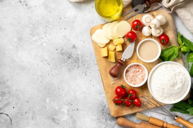 Pizza ingredients on a culinary background. Flour, yeast, salt, water, olive oil, parmesan, cheese, mozzarella, basil, tomatoes on the table. The concept of preparing for baking pizza or pie. Top view