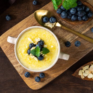 Yaban mersinli ve bademli Polenta yemeği. Kahverengi ahşap mutfak masasında seramik tabakta mısır lapası. Sütlü krema çorbası. Sağlıklı vejetaryen yemekleri