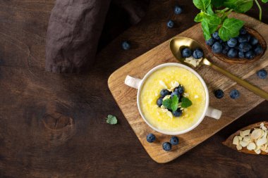 Yaban mersinli ve bademli Polenta yemeği. Kahverengi ahşap mutfak masasında seramik tabakta mısır lapası. Sütlü krema çorbası. Sağlıklı vejetaryen yemekleri. Üst görünüm