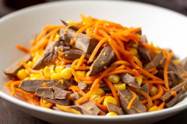 Kahverengi ahşap arka planda bir tabakta hindi kalbi, havuç ve mısır salatası. Sağlıklı beslenme