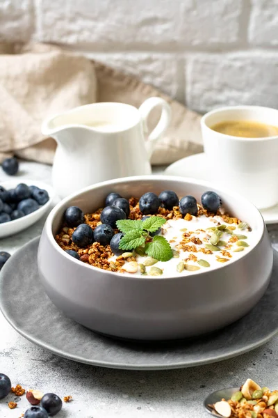 Homemade organic buckwheat granola with yogurt, blueberries, hazelnuts, peanuts, nutmeg, pumpkin seeds and flax seeds in a ceramic bowl on a light background. Breakfast for healthy