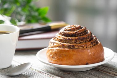 Beyaz tabakta haşhaş tohumlu ekmek ve masada bir fincan kahve. Kahve molası ya da çörekle kahvaltı.