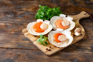 Kahverengi ahşap bir masada servis tahtasındaki kabukta çiğ deniz tarağı. 