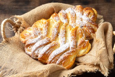 Süzme peynirli tatlı bir çörek ve kahverengi ahşap bir masanın üzerinde sepetin içinde kuru üzüm. Ev yapımı yüksek kalorili pişirme konsepti