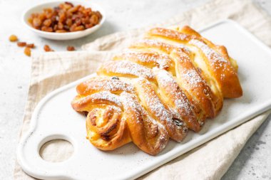 Süzme peynirli tatlı çörek ve servis tahtasındaki kuru üzümler yakın plan beyaz mutfak masasında. Ev yapımı yüksek kalorili hamur işleri.
