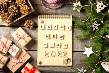 Mutlu yıllar. 2022 numara kahverengi ahşap zemin üzerinde ahşaptan yapılmıştır. Noel arka planında köknar dalları, ahşap dekorlar ve el işi kağıdından hediye kutularıyla süslenir. Düzgünce