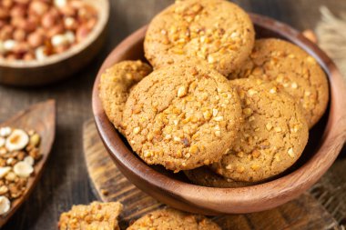 Sağlıklı ev yapımı yulaf ezmeli kurabiyeler. Kahverengi mutfak masasının üzerinde, ahşap bir kasede fıstık var.