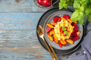 Geleneksel klasik Belçika ya da Brüksel waffleları mavi ahşap mutfak arka planında kırmızı erikli bir tabakta