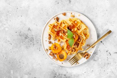 Geleneksel klasik Belçika ya da Brüksel waffle 'ı kayısı reçeli ve açık gri mutfak masasında seramik tabakta ceviz.